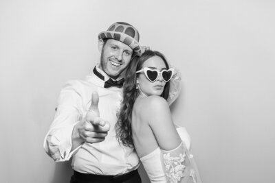 bride and groom wearing props, posing against a white backdrop, with a Kardashian glam filter, during the wedding party entertainment photo booth hire and rental