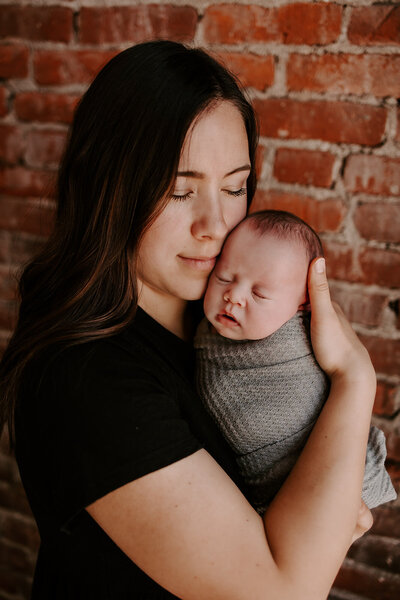 mom by a brick wall holding newborn baby girl