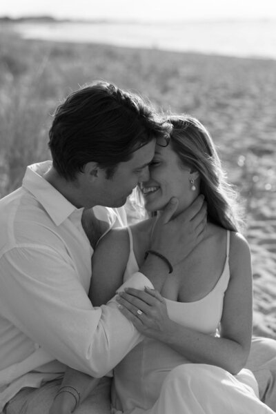 A couple sitting on Steps beach on Nantucket with the man pulling his fiancee in for a kiss