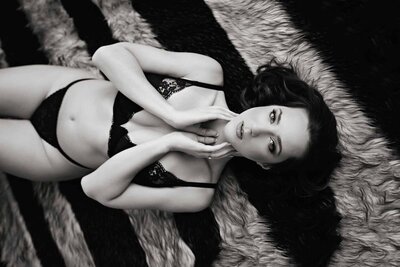 Black and white sultry boudoir portrait of woman posed on black and grey striped rug