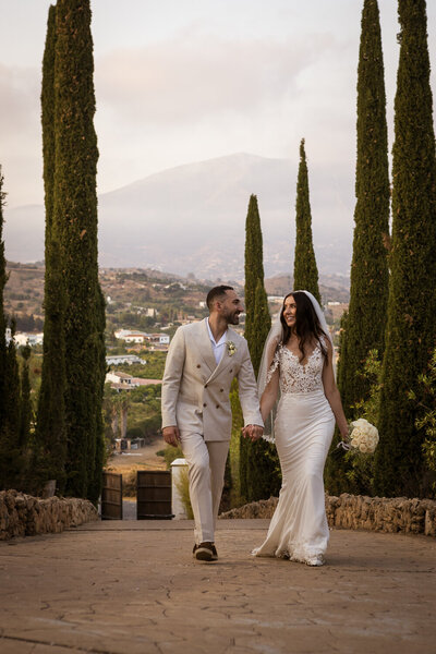 Bride and groom walking down a typical mediteranean  pathe surrounded by Cyprus trees.