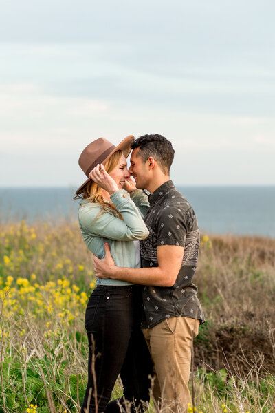 Couple embraces eachother while standing in a flower field on the coast of california.