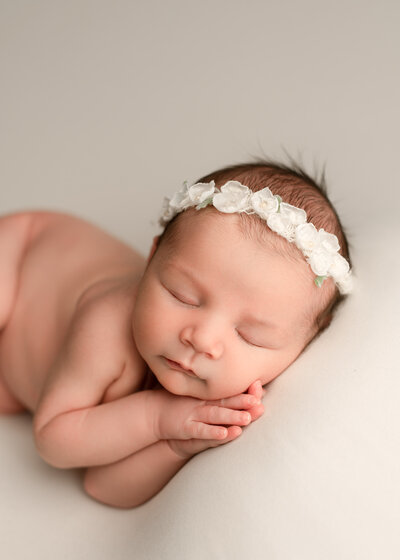baby girl sleeping on a white blanket wearing a white flower headband
