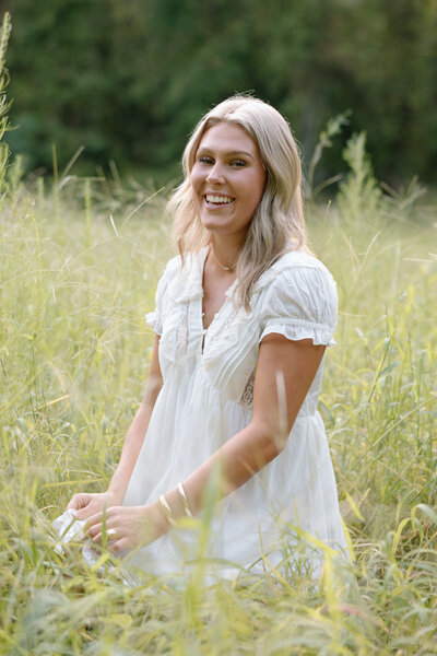 Senior sits in a tall fiels of grass while laughing