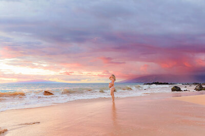 Pregnant Maui woman photographed at the beach at sunset wearing a bikini