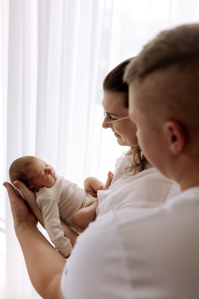 Ein Paar hält ihr Baby vor sich und schauen es an
