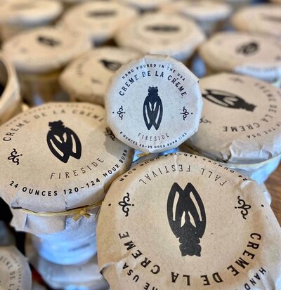 Stacks of round, paper-wrapped packages labeled "Crème de la Crème," designed by Sweet Pea Ink Creative, with a central black graphic and product details printed on the top—perfect for elevating your brand’s visual identity.