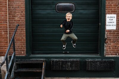 Family photographer Pittsburgh captures a child jumping off steps in front of a closed green door with a "closed for lunch" sign.