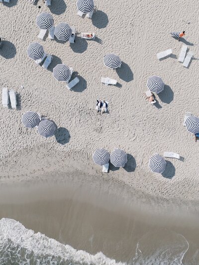 Drone photo of two grooms laying down on the beach surrounded by umbrellas in Cape May NJ