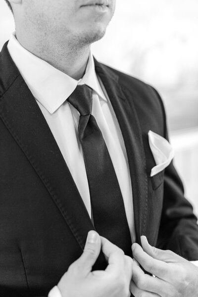Black and white close-up of groom adjusting tie and suit lapel at Lido House, Newport Beach