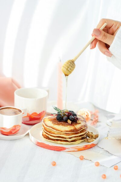 Stack of pancakes with honey and berries representing food freedom and intuitive eating principles in eating disorder recovery nutrition