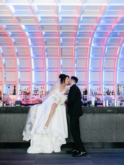 Bride sits on bar and leans over to kiss groom at Hotel washington