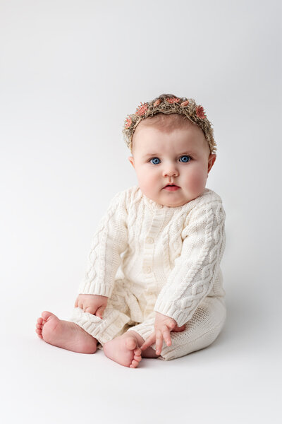This elegant milestone portrait features a baby girl styled in soft neutrals, surrounded by timeless textures and gentle light.