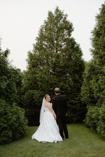 Classic photo of groom facing away from the camera while the bride looks over her shoulder at the camera