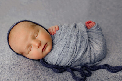 newborn boy swaddled in navy blue sleeping in a moon shaped wooden prop for his york newborn photo session