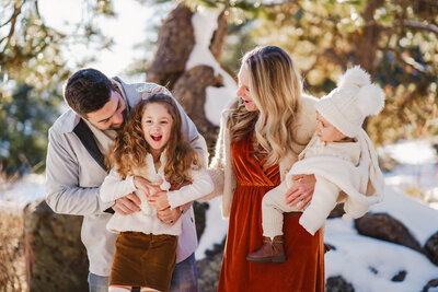 Denver Family Photographers capture children laughing while mom kisses baby
