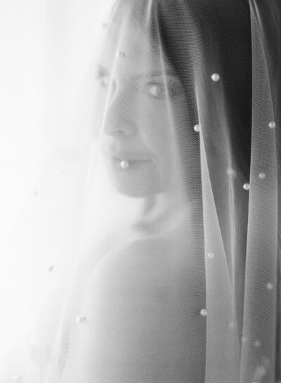 A bride with a veil on her head looks at the camera.