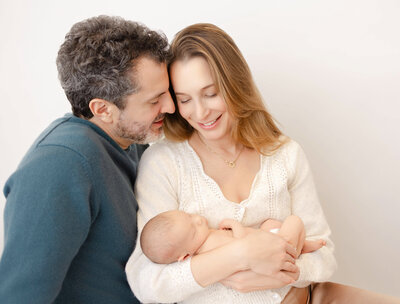 new parents holding baby girl in arms against a white backdrop at Heather Nicole Photography Studio.