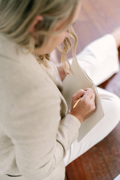 A woman sitting on a wood floor, writing in a notebook.