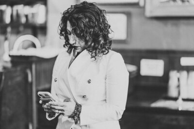 Black and white image of woman in white blazer looking down at her cell phone
