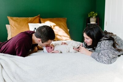 Mother and father with newborn baby on bed as dad kisses baby