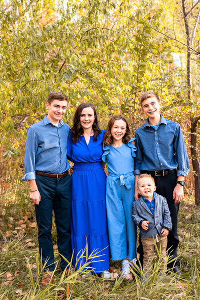 Five siblings pose for a photo in front of fall leaves.