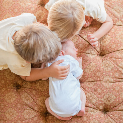 Older brothers kissing newborn brother in Carmel Valley Ranch home