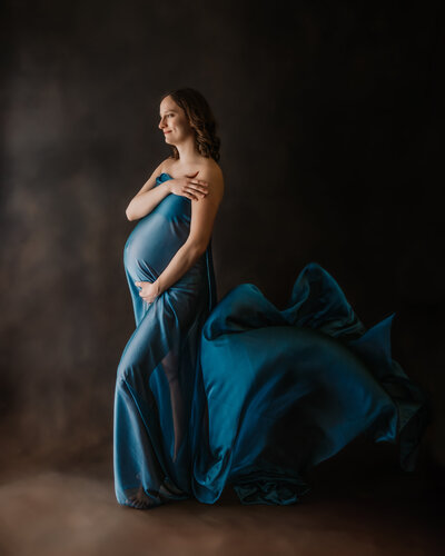 pregnant mom to be is wrapped in a blue flowing fabric to show off her bumb