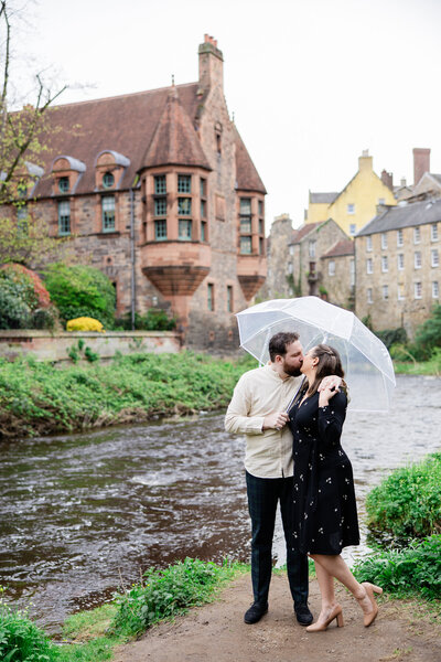 bride and groom kiss under umbrella on riverbank