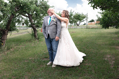 Bride sneaking up on groom in Apple Orchard for first look.