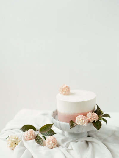 pastel pink cake covered in flowers on a cake stand