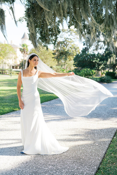 Bride throws veil into the wind on the path of Jekyll Island Club Resort during wedding weekend