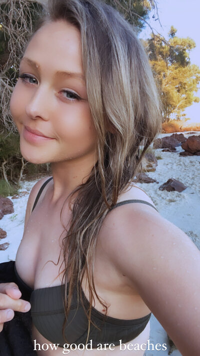 Blonde girl softly smiling at camera taking a selfie in swimwear on the beach