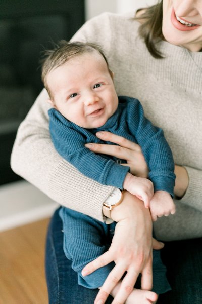 An in-home Rochester NY newborn photography session, in which a newborn baby smiles in his mother's arms.