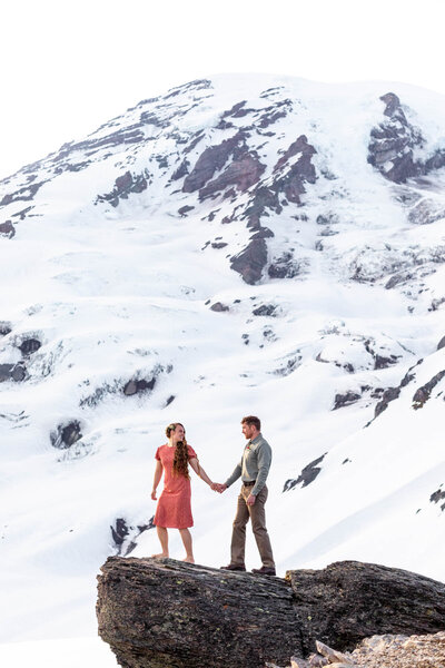 bride is holding grooms hand as she leads the way with mt rainier behind them
