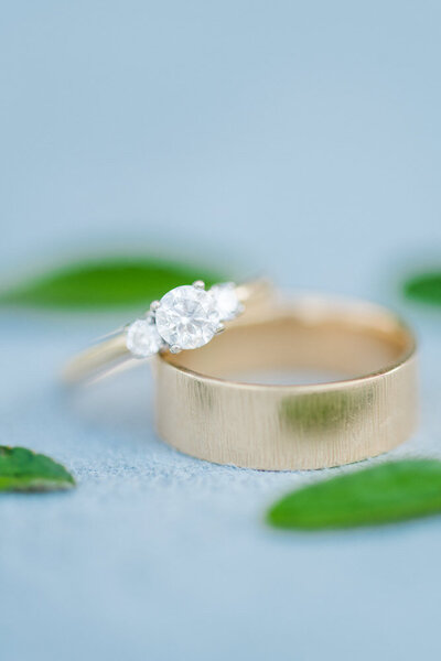 wedding rings on blue fabric surrounded by green leaves