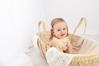 1 year old girl sitting in Moses basket