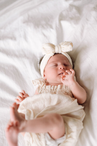Newborn baby wearing a soft linen outfit and bow headband resting peacefully on a bed, photographed by a Northern Virginia family photographer.