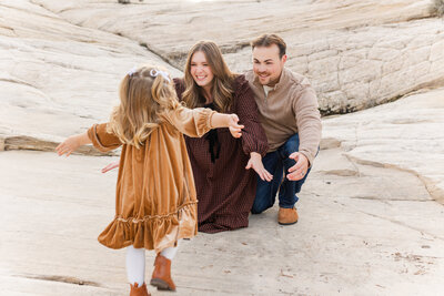 dad holding little girl up in the air and little girl is smiling at her mom