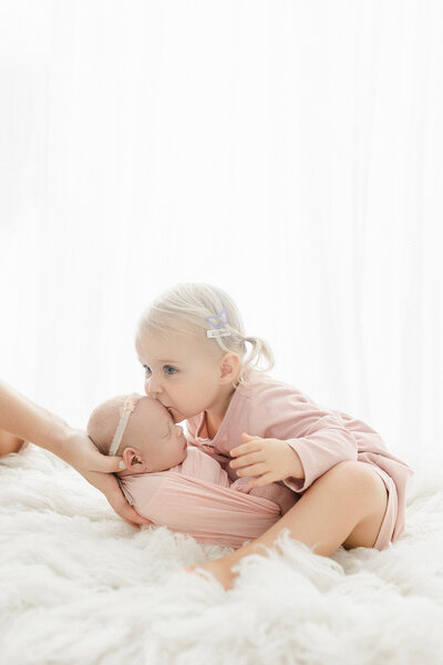 A toddler girl kissing her newborn baby sister during their in-home session in Grand Forks, ND. 