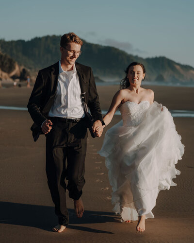 a bride and groom holding hands while running on the beach