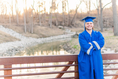 senior boy in cap and gown on bridge