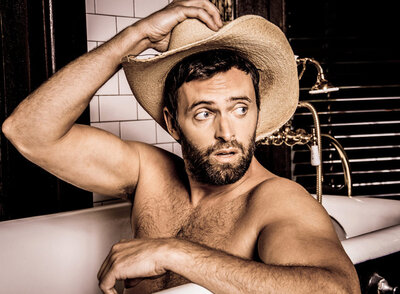 Country Music portrait of Dean Young sitting in bathtub shirtless holding his cowboy hat