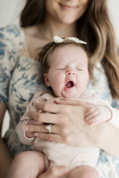 Close-up of a newborn baby yawning while being held by their mother in a floral dress during a Kansas City newborn session.
