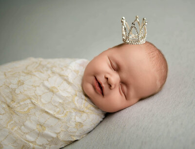 newborn baby swaddled with a tiny crown on her head