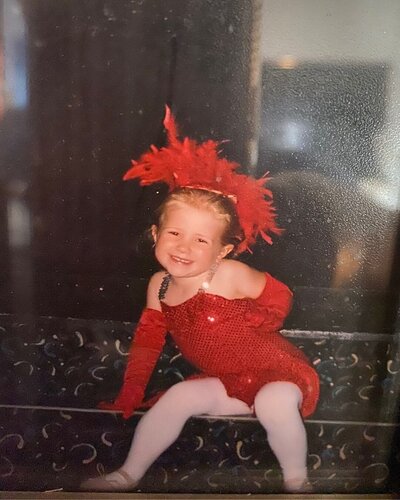 Baby photo of Autumn the wedding photographer sitting on steps in a red flashy dance costume