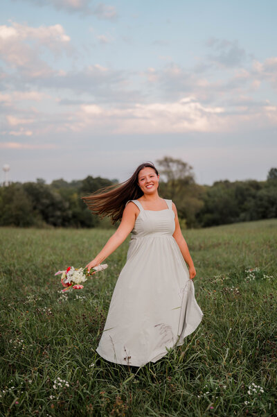 Teenage girl poses for the camera outside standing in an open field with wildflowers in her hands.