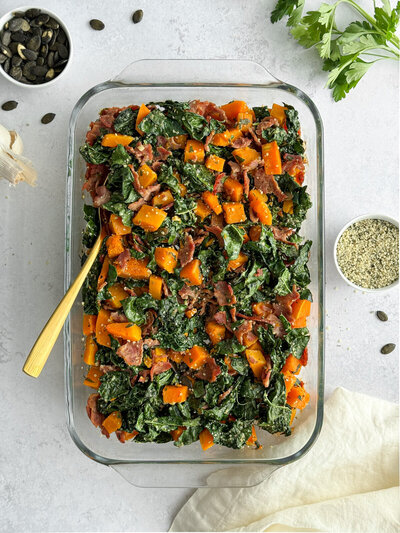 A butternut squash casserole with kale, turkey bacon, hemp seeds and pumpkin seeds sprinkled on top.