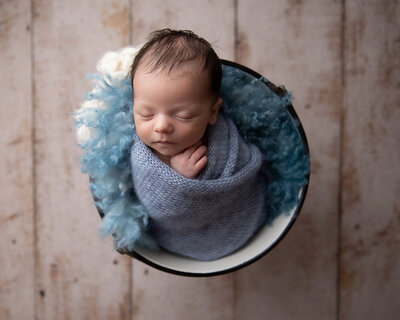 newborn boy swaddled in blue wrap in bucket
