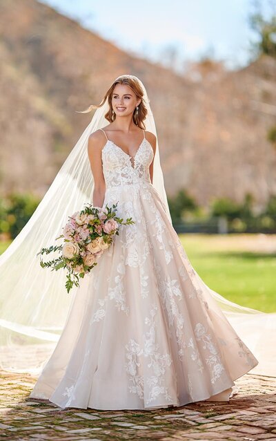 ROMANTIC BOHO A-LINE WEDDING DRESS WITH POCKETS With a dramatic statement worthy of a boho goddess, this full A-line wedding dress is soft, sweet and all-natural. Large-scale floral laces are placed throughout the gown with touches of soft beading for a subtle shimmer. Beaded shoestring straps extend from the organic V-neckline into an all-out strappy back for a distinctly bohemian feel! Also available in a matte option, this romantic style still shines with negative space elements over blush or neutral lining, and pockets in the full skirt for a modern touch.